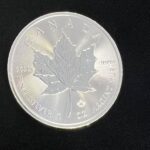 A silver maple leaf coin is shown on the black background.